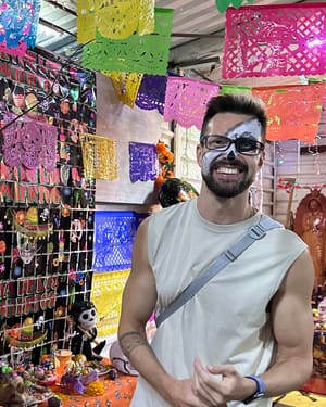 Andrey in calavera face paint at a Día de Muertos market stall hung with papel picado
