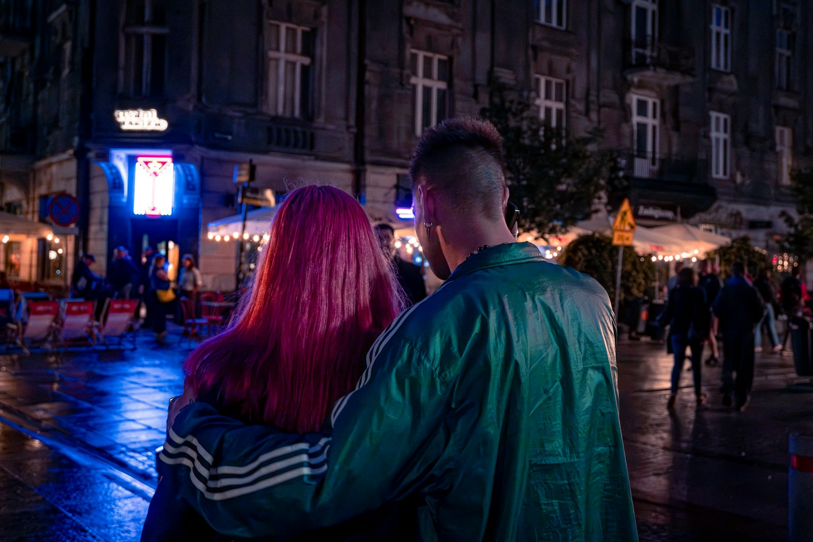 A couple walking through a neon-lit street at night.