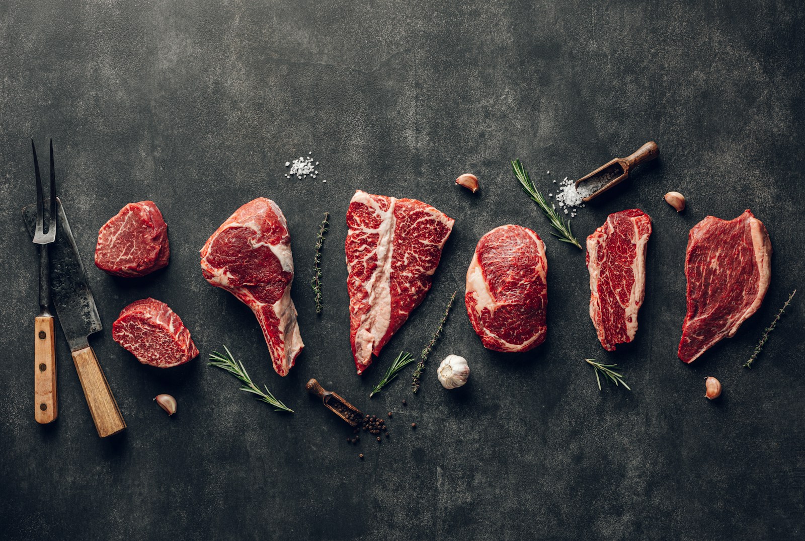 Raw beef cuts of different thicknesses arranged on a dark surface.