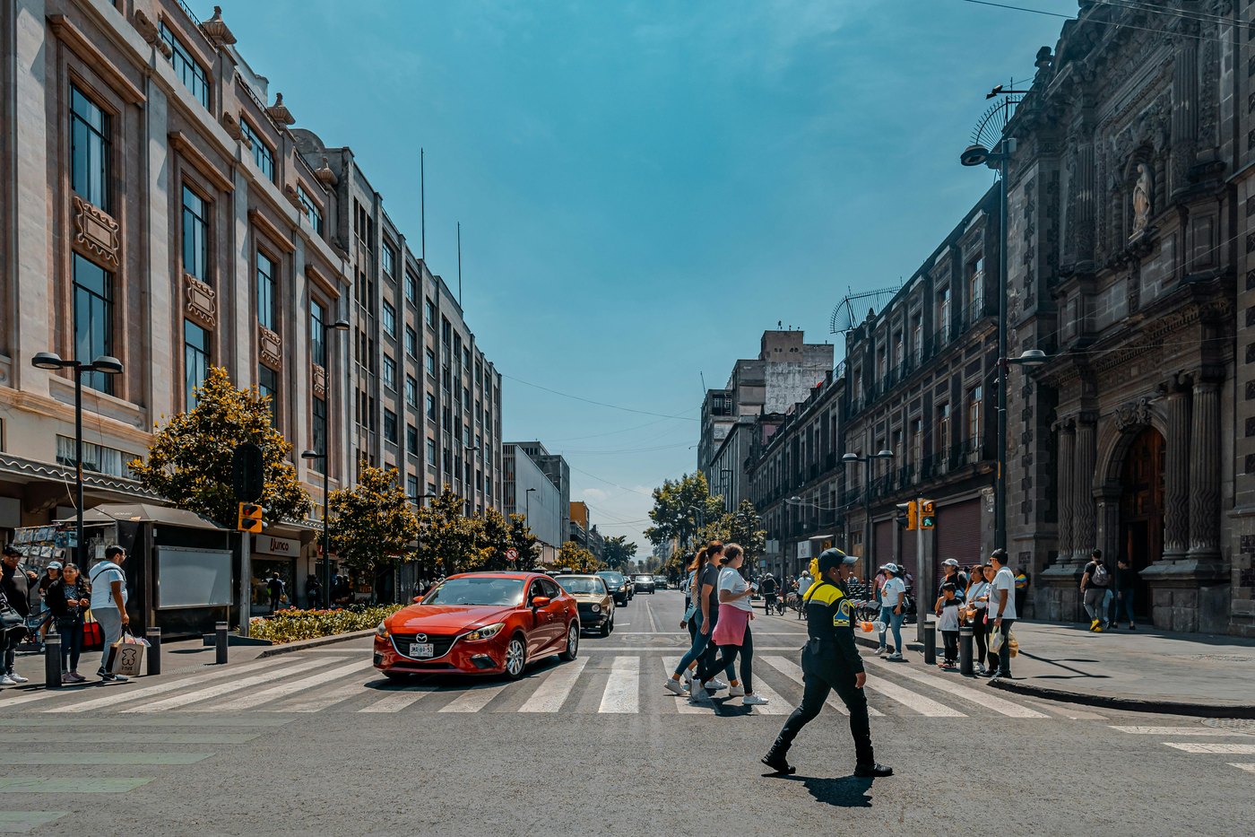 People crossing a busy street in Mexico City in warm afternoon light.