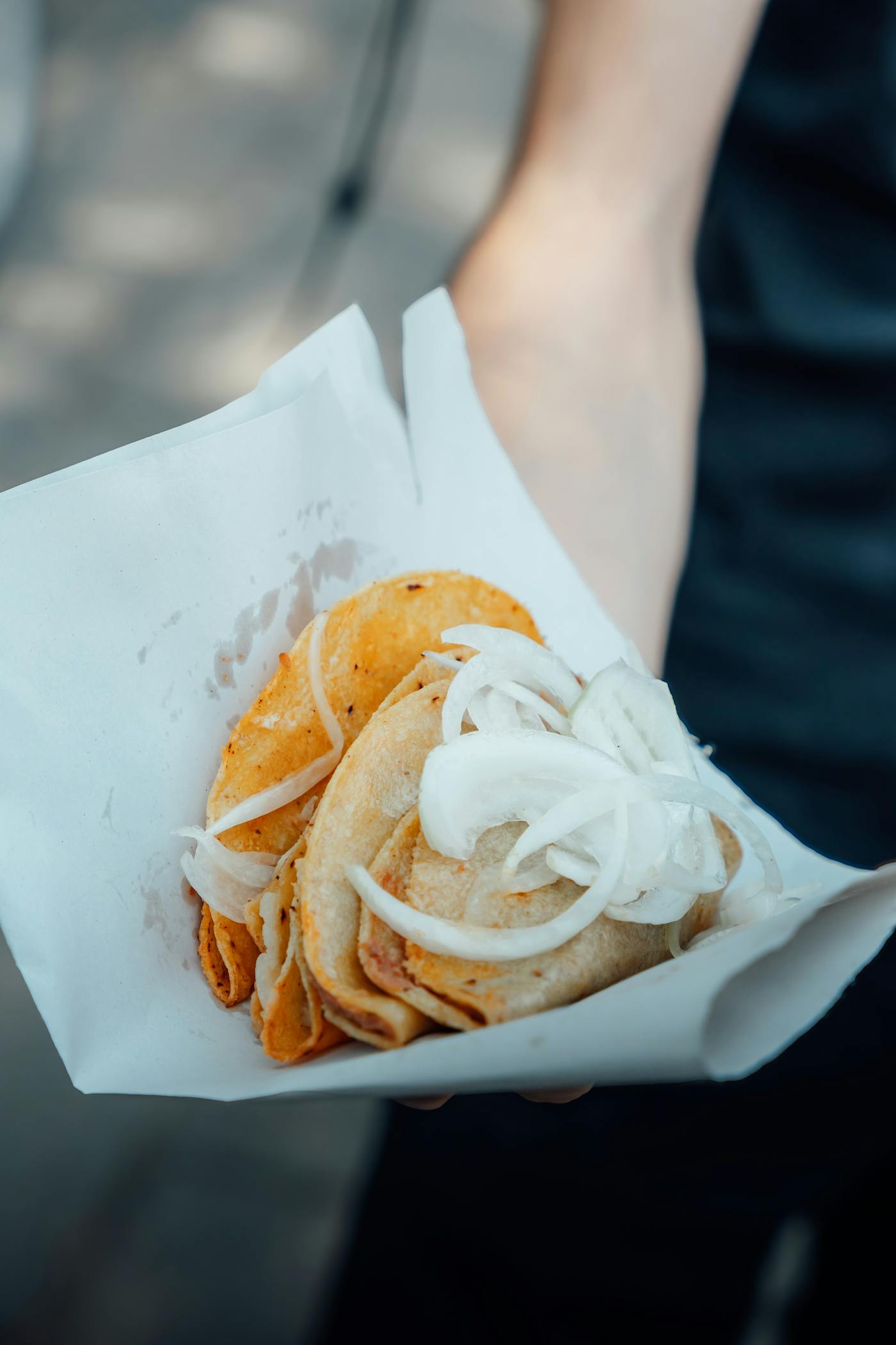 A hand reaching for tacos at a Mexican street food stand.