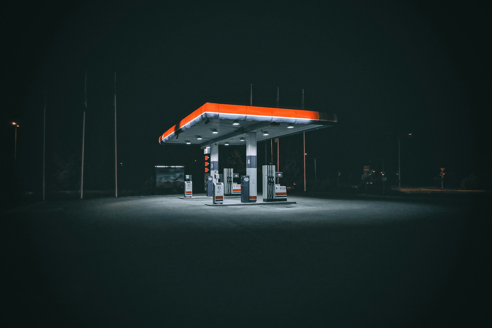 A brightly lit petrol station forecourt at night, with pump islands glowing under a wide canopy.