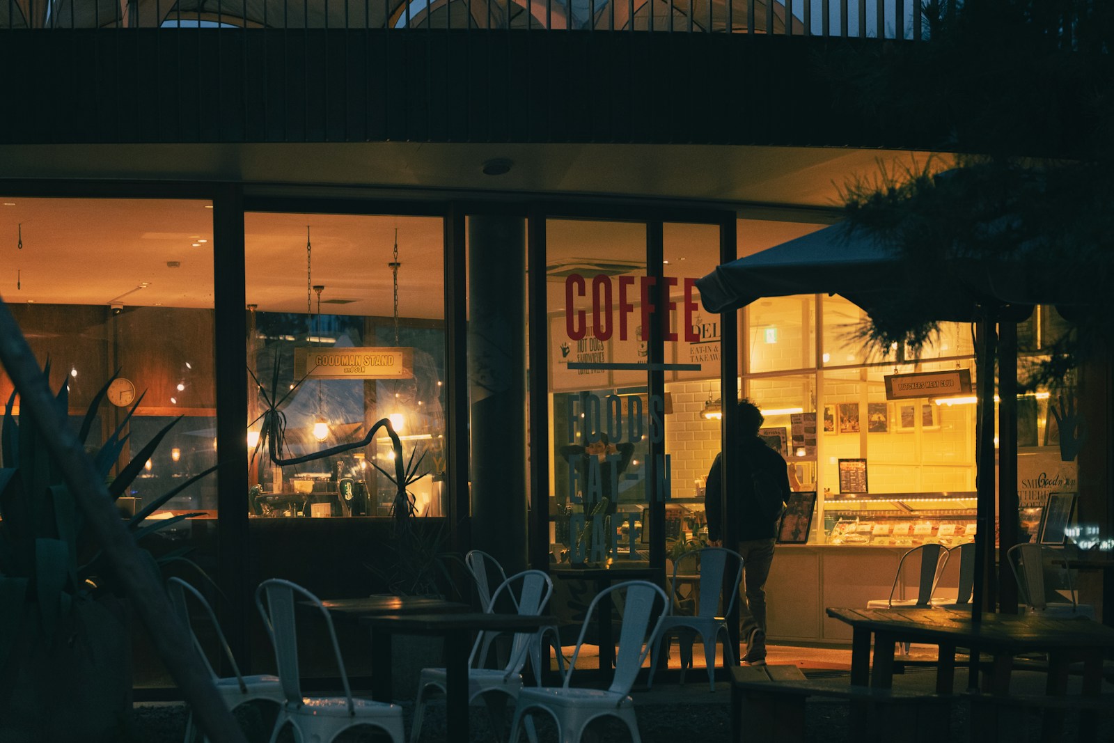 A person sitting alone by the lit window of a coffee shop at night.