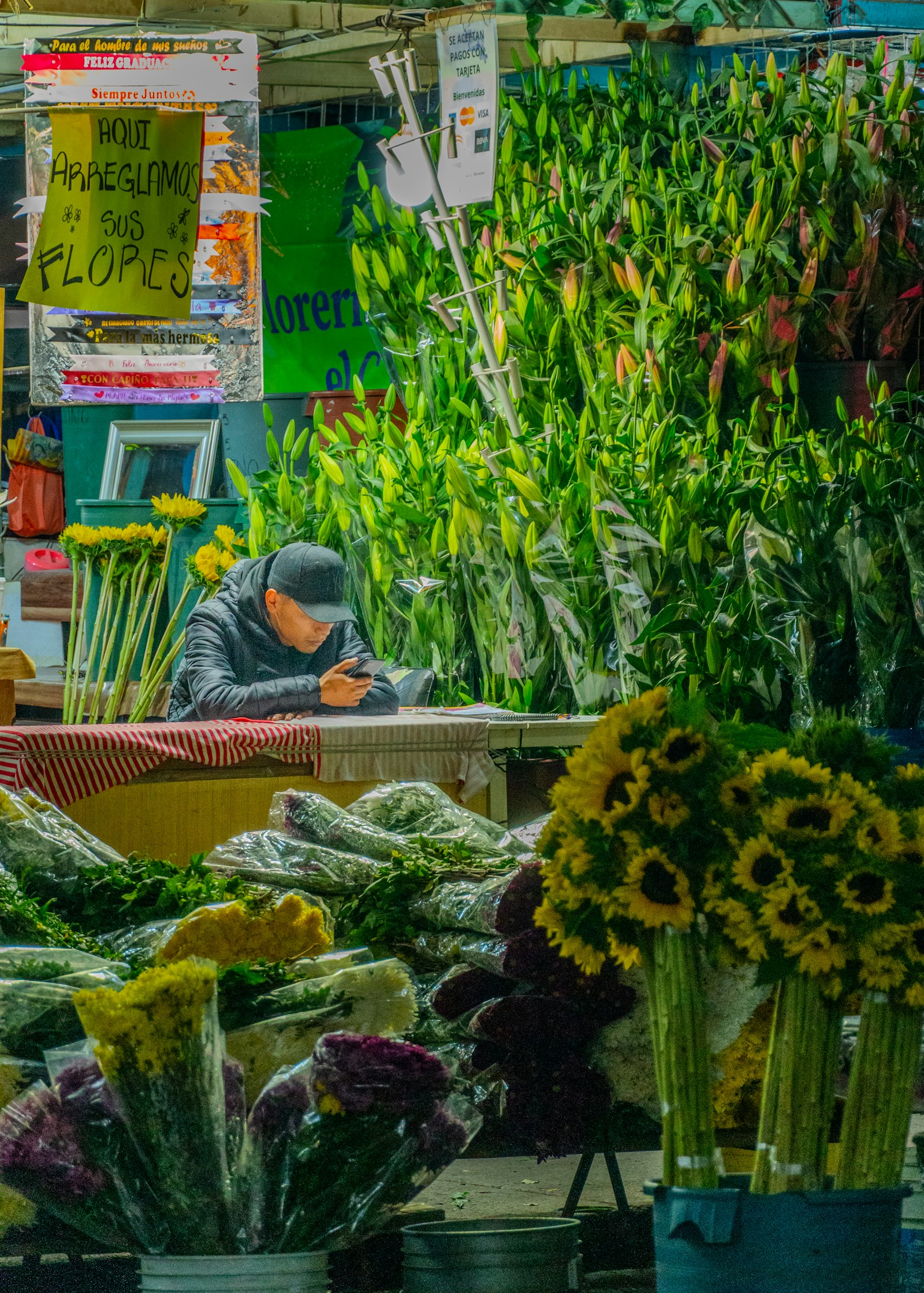 A vendor almost hidden among tall green flower stems at a densely packed stall.