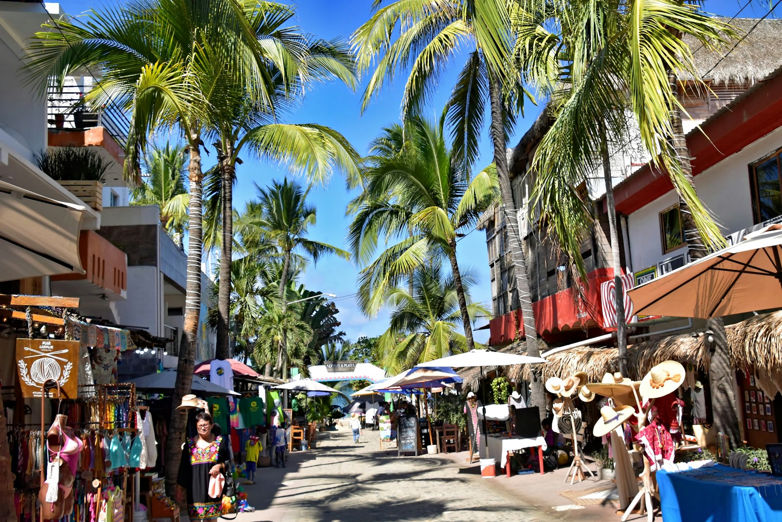 An open-air market street lined with shopfronts and palm trees.