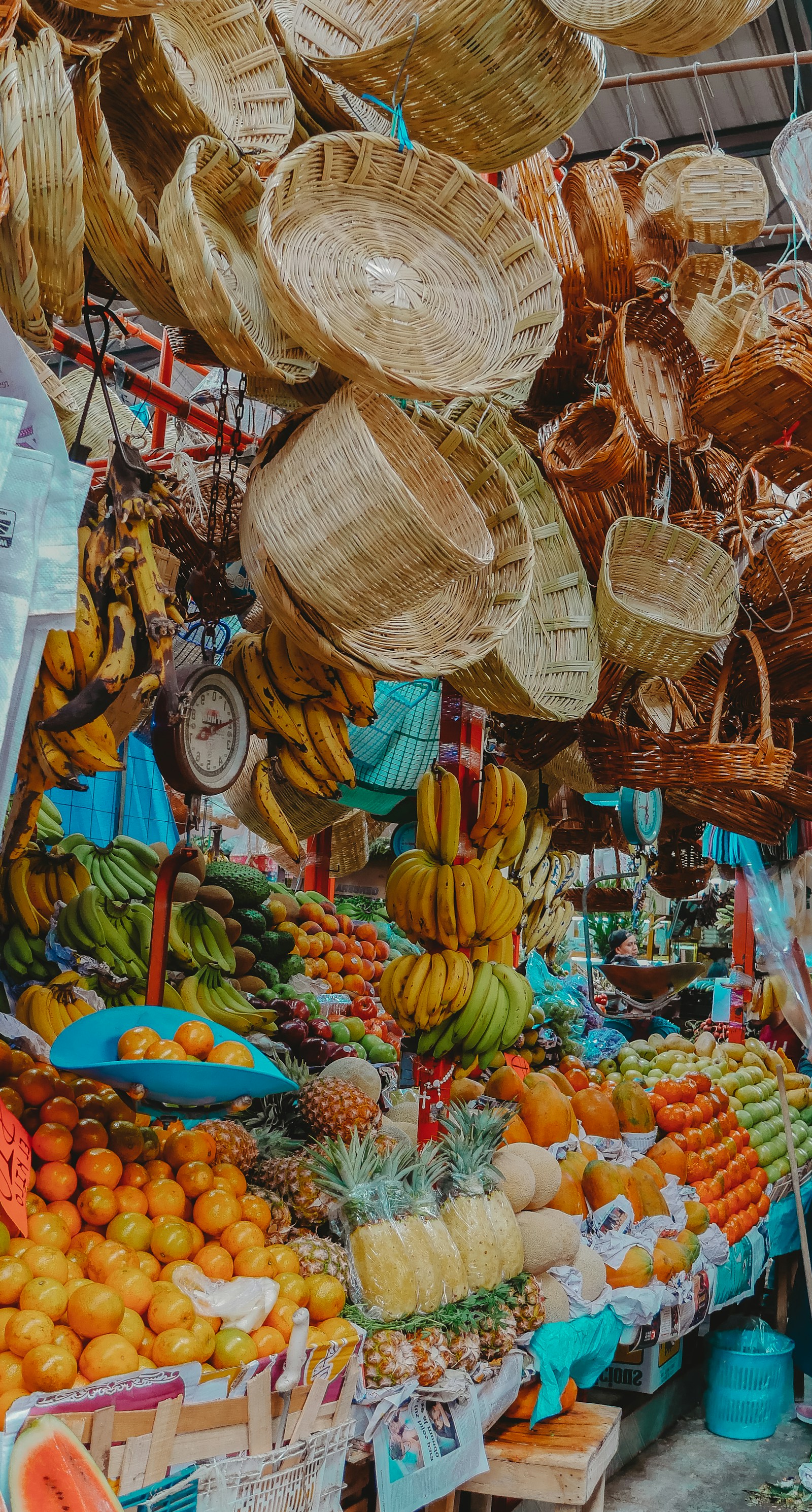 Woven baskets hanging above crates of oranges and other fruit at a market stall.