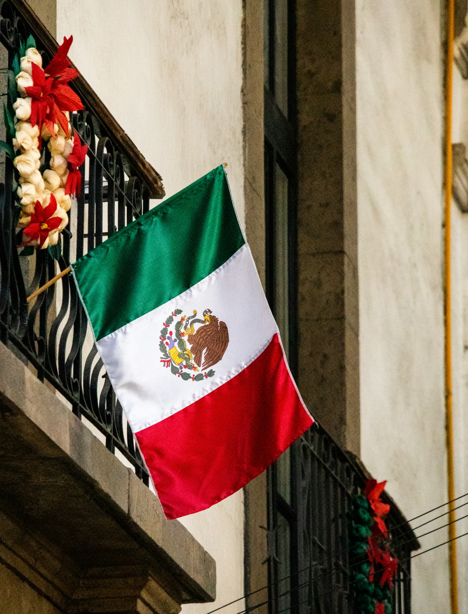 A Mexican flag hanging from the balcony of a building.