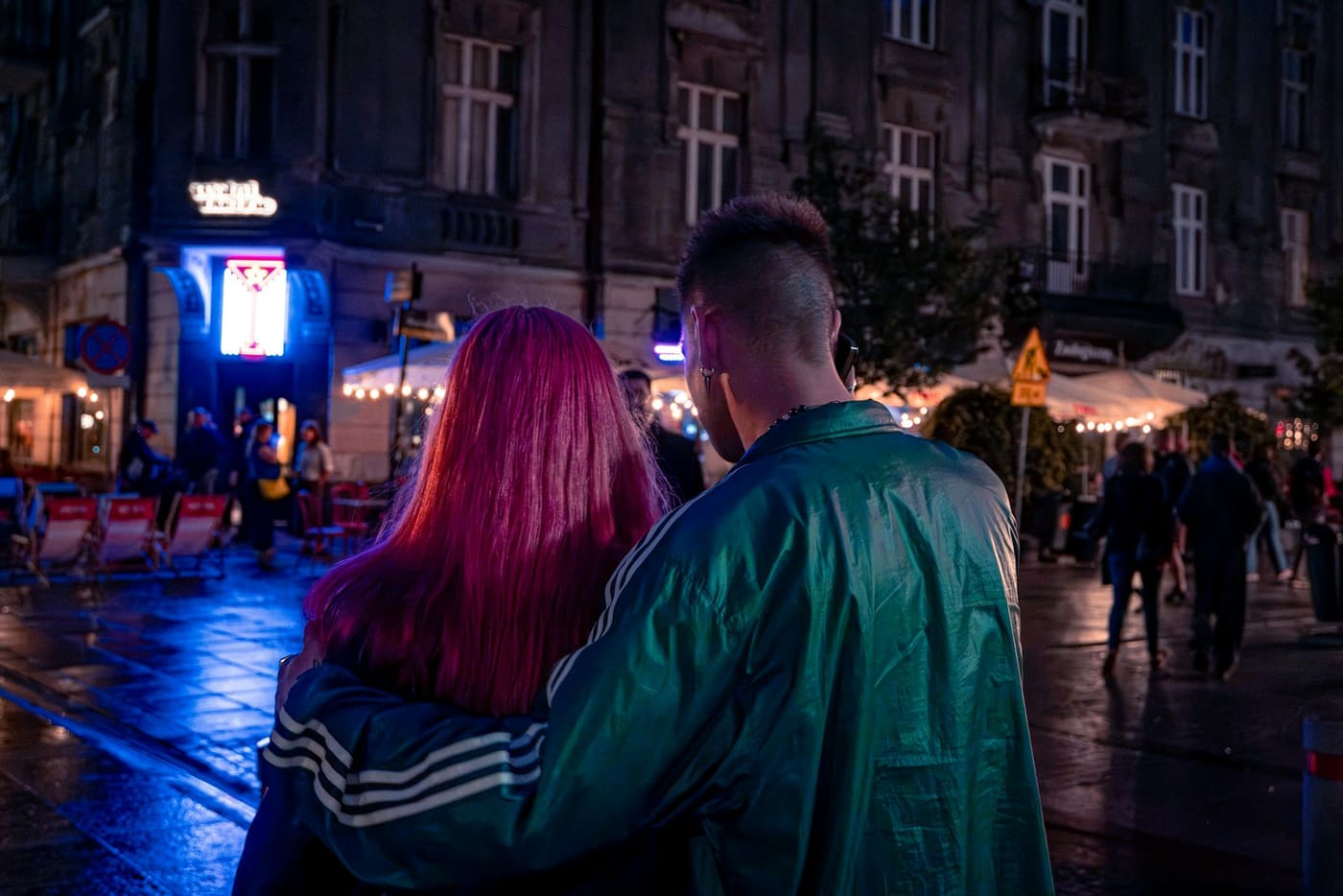 A couple walking through a neon-lit street at night.