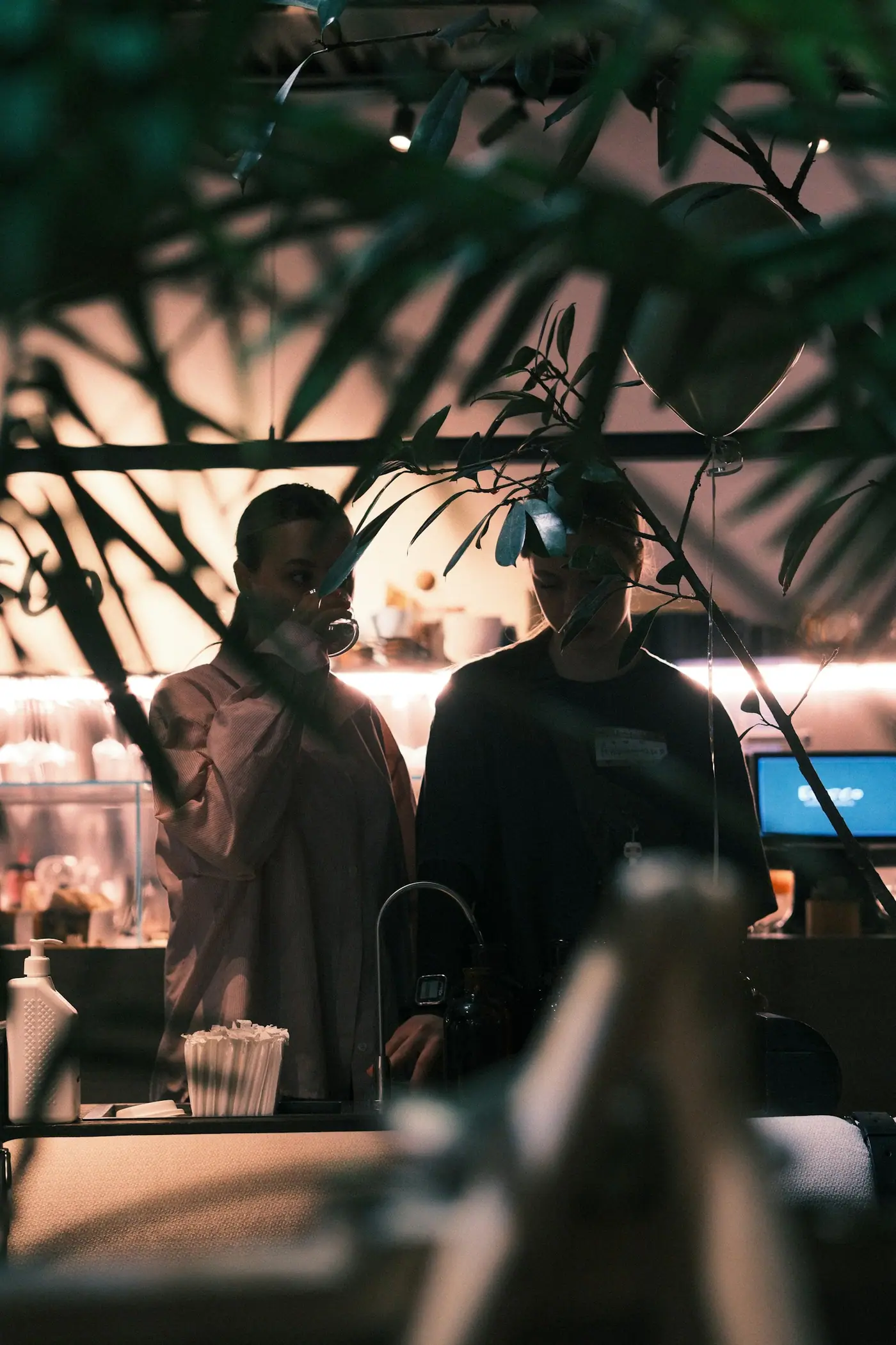 Two people standing together in a dimly lit bar with warm background lights.