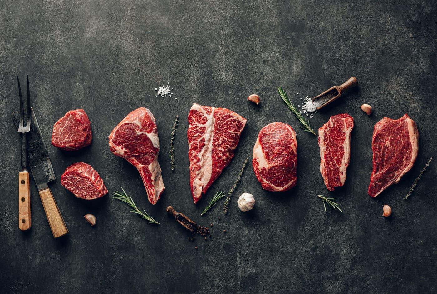 Raw beef cuts of different thicknesses arranged on a dark surface.