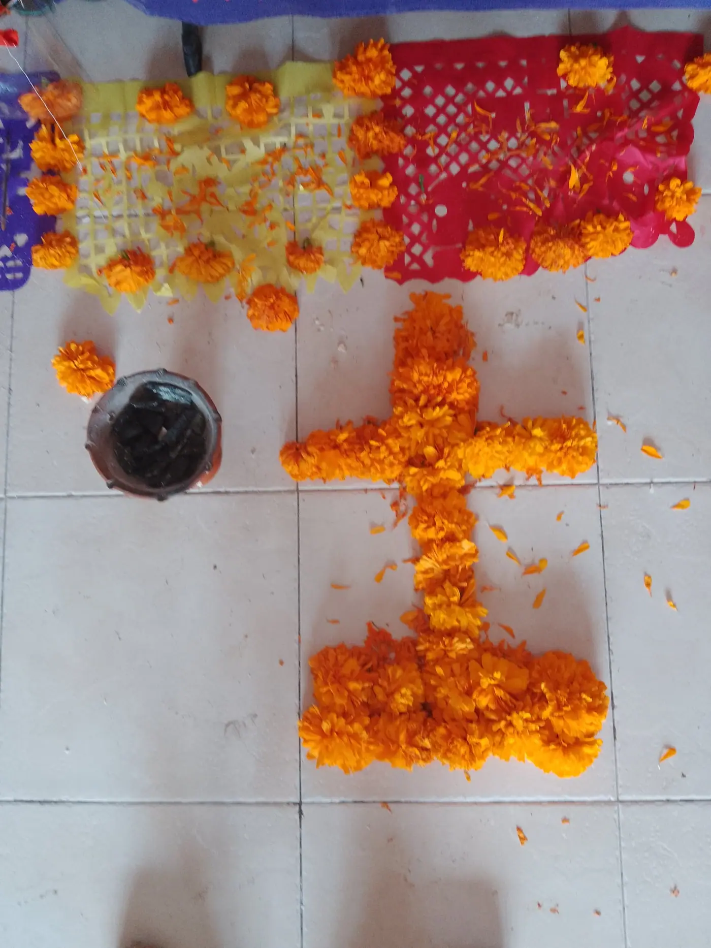 A cross laid out in loose marigold petals on a tiled floor