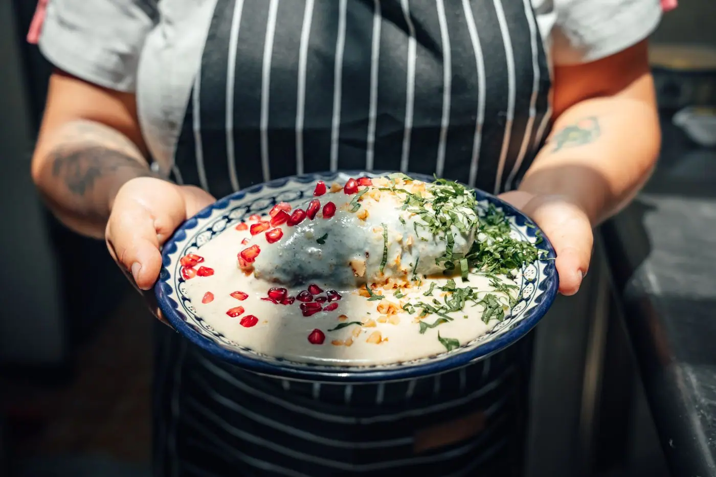 A plate of chiles en nogada topped with walnut cream sauce and red pomegranate seeds.