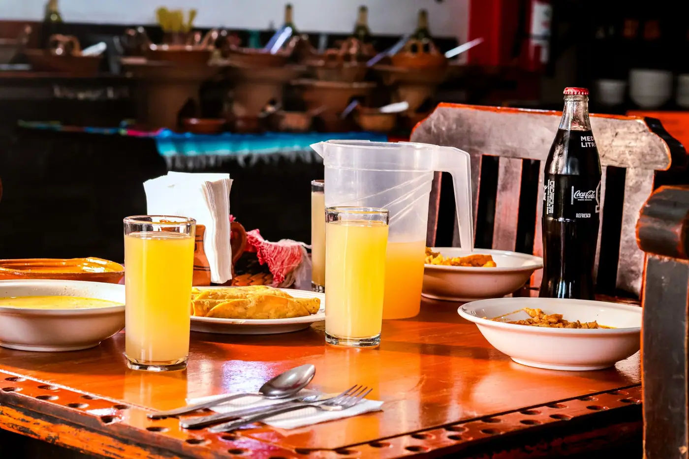 A fonda table set with soup, a plated main, two glasses of agua fresca and a bottle of Coca-Cola