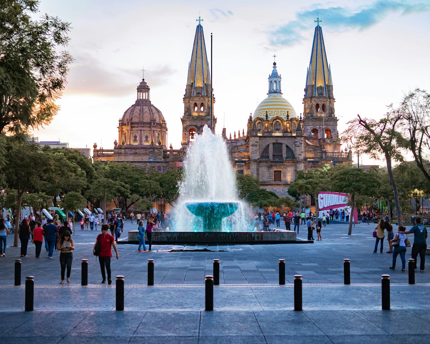 People gathered near a fountain in a shaded public square.