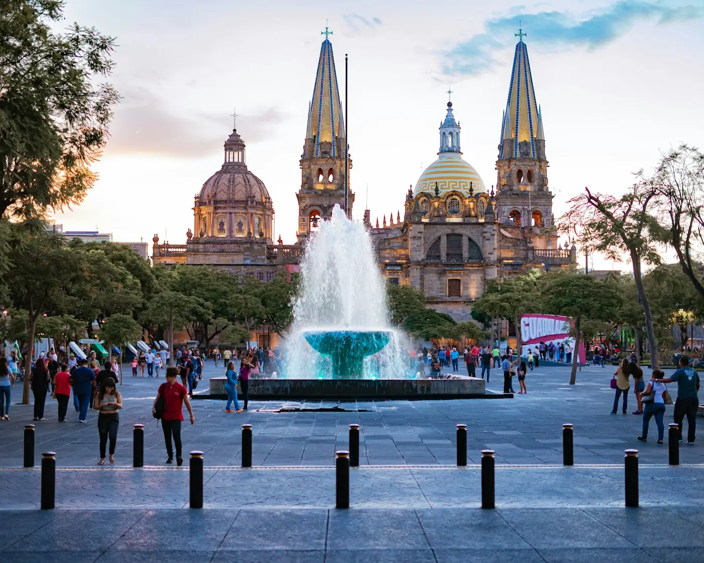 People gathered near a fountain in a shaded public square.