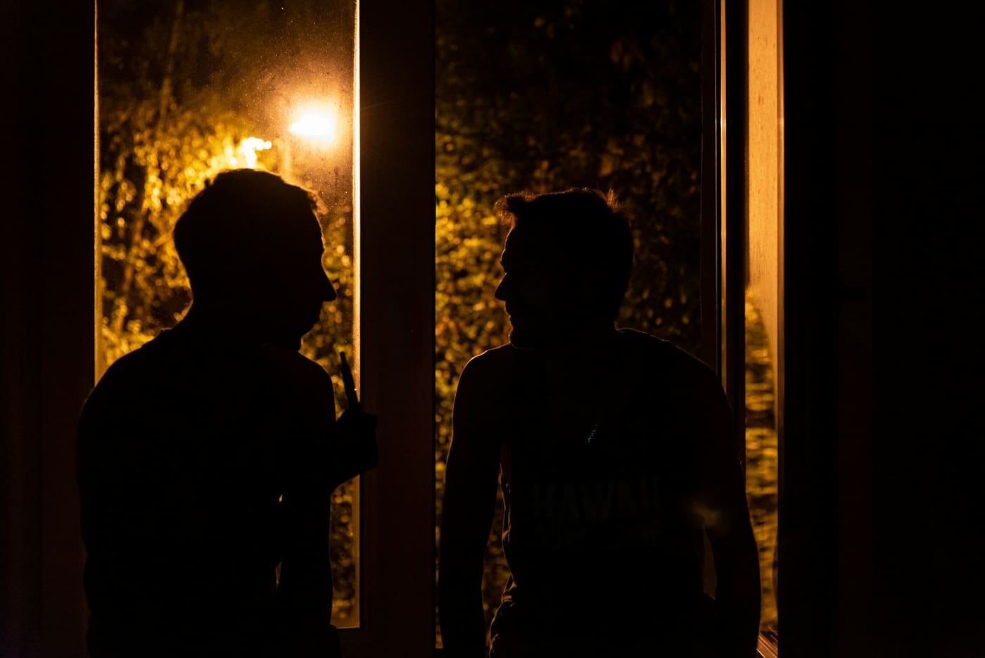 Two people talking in silhouette in a doorway at night, lit from behind.