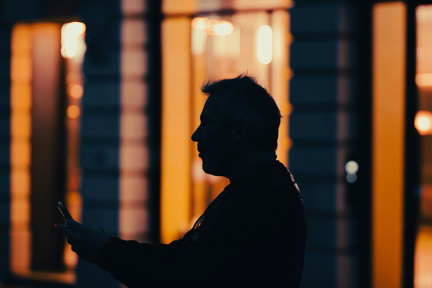 A person in silhouette against the warm lit windows of a building at night.