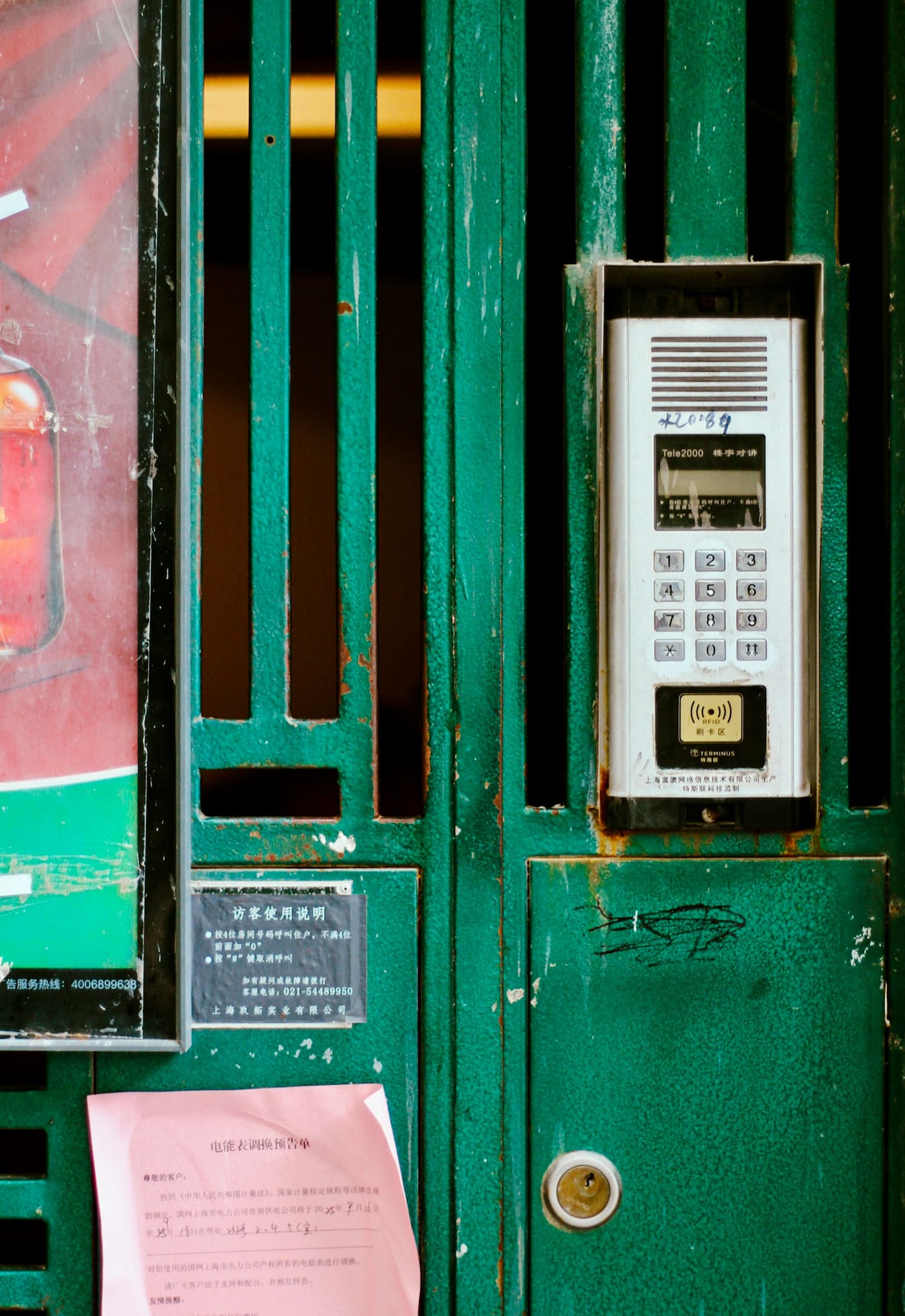 A green metal gate with an intercom keypad panel and a posted notice beside it.