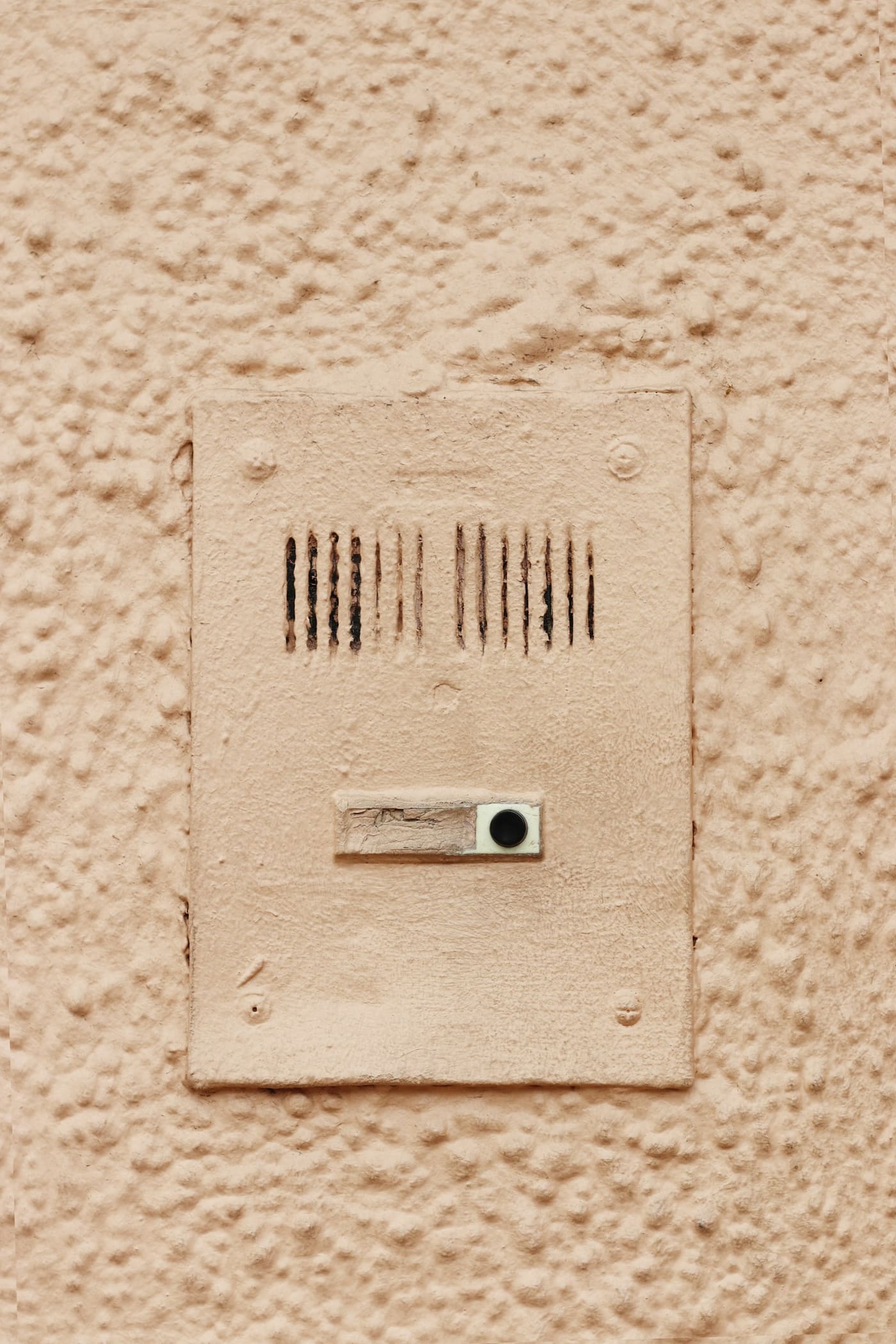 A cream-colored intercom speaker and button unit mounted on a textured painted wall.