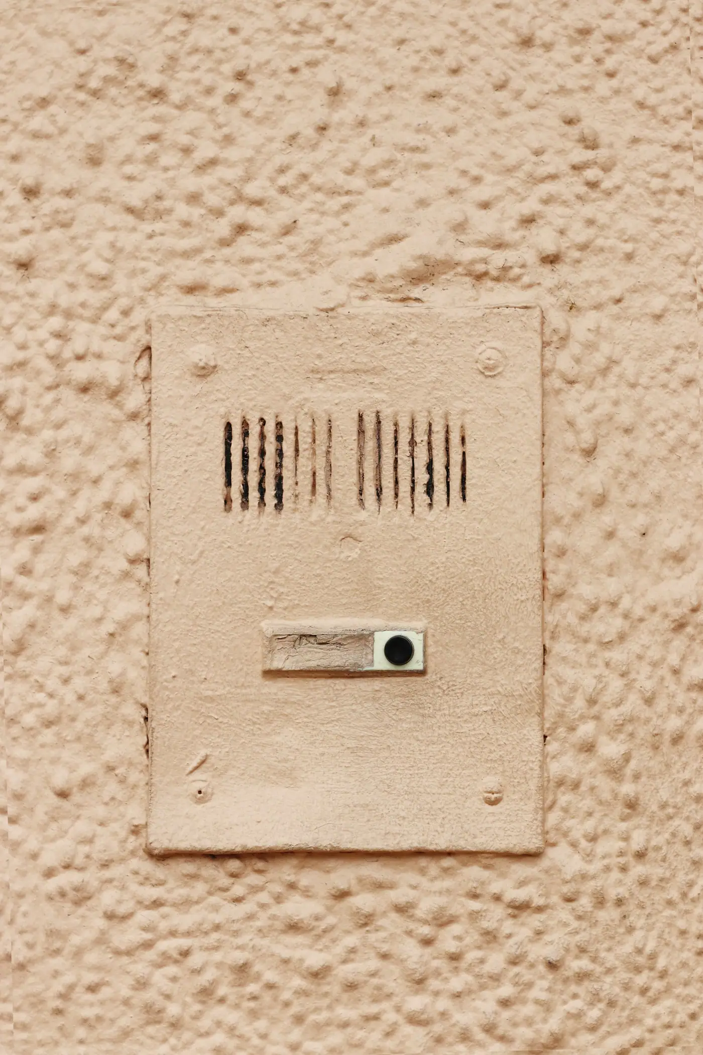 A cream-colored intercom speaker and button unit mounted on a textured painted wall.