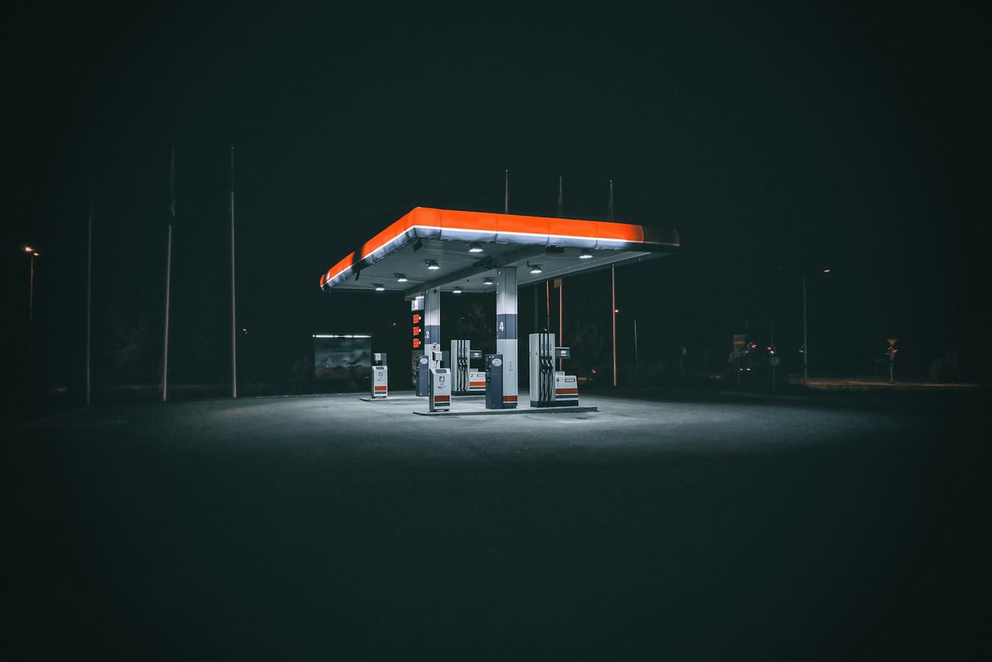 A brightly lit petrol station forecourt at night, with pump islands glowing under a wide canopy.