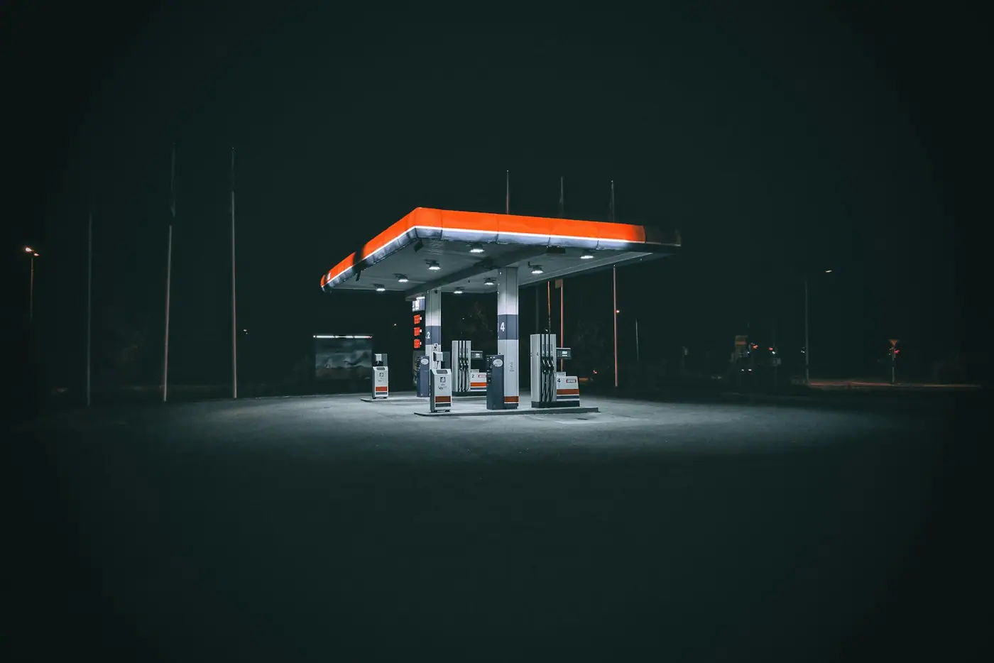 A brightly lit petrol station forecourt at night, with pump islands glowing under a wide canopy.
