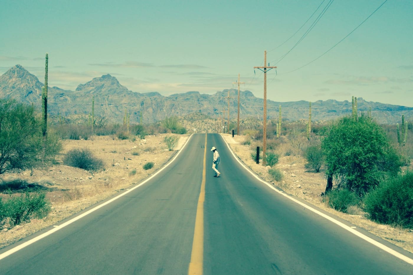 An empty two-lane highway running straight toward dry hills under an open sky.