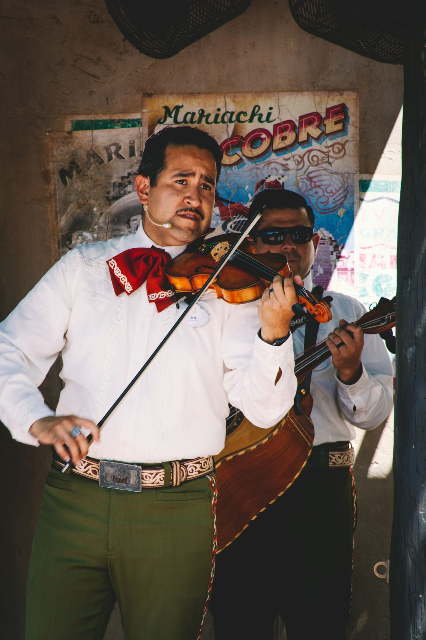 A musician playing a violin with another person standing behind him.