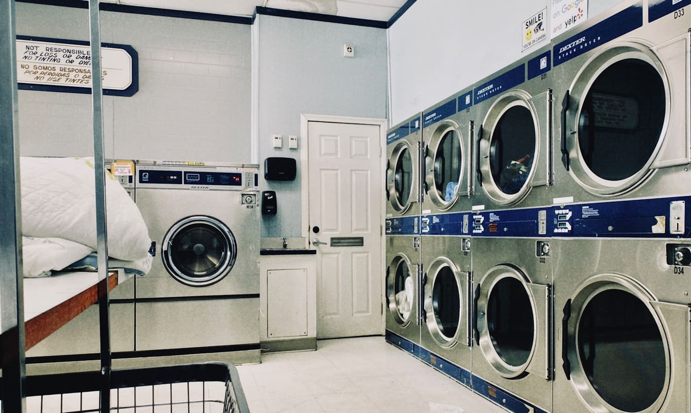 A row of front-loading washing machines and dryers along the wall of a laundry room.