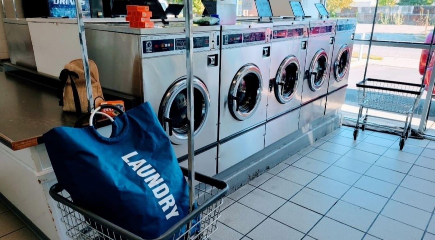 A laundry bag in a wire cart in front of a row of commercial washing machines.