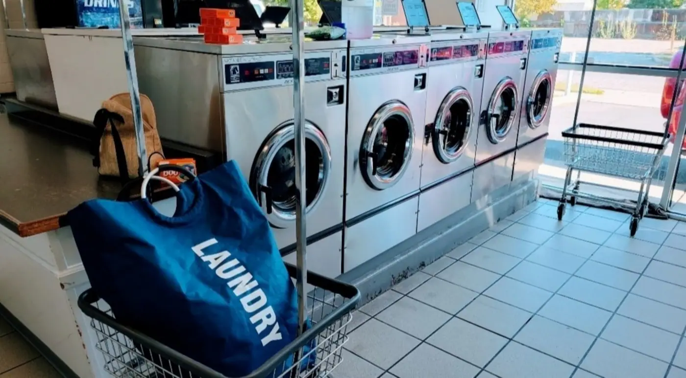 A laundry bag in a wire cart in front of a row of commercial washing machines.