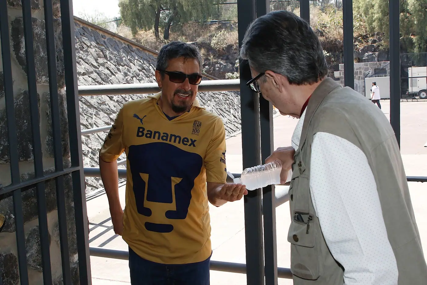 Two men talking, one wearing a Pumas shirt