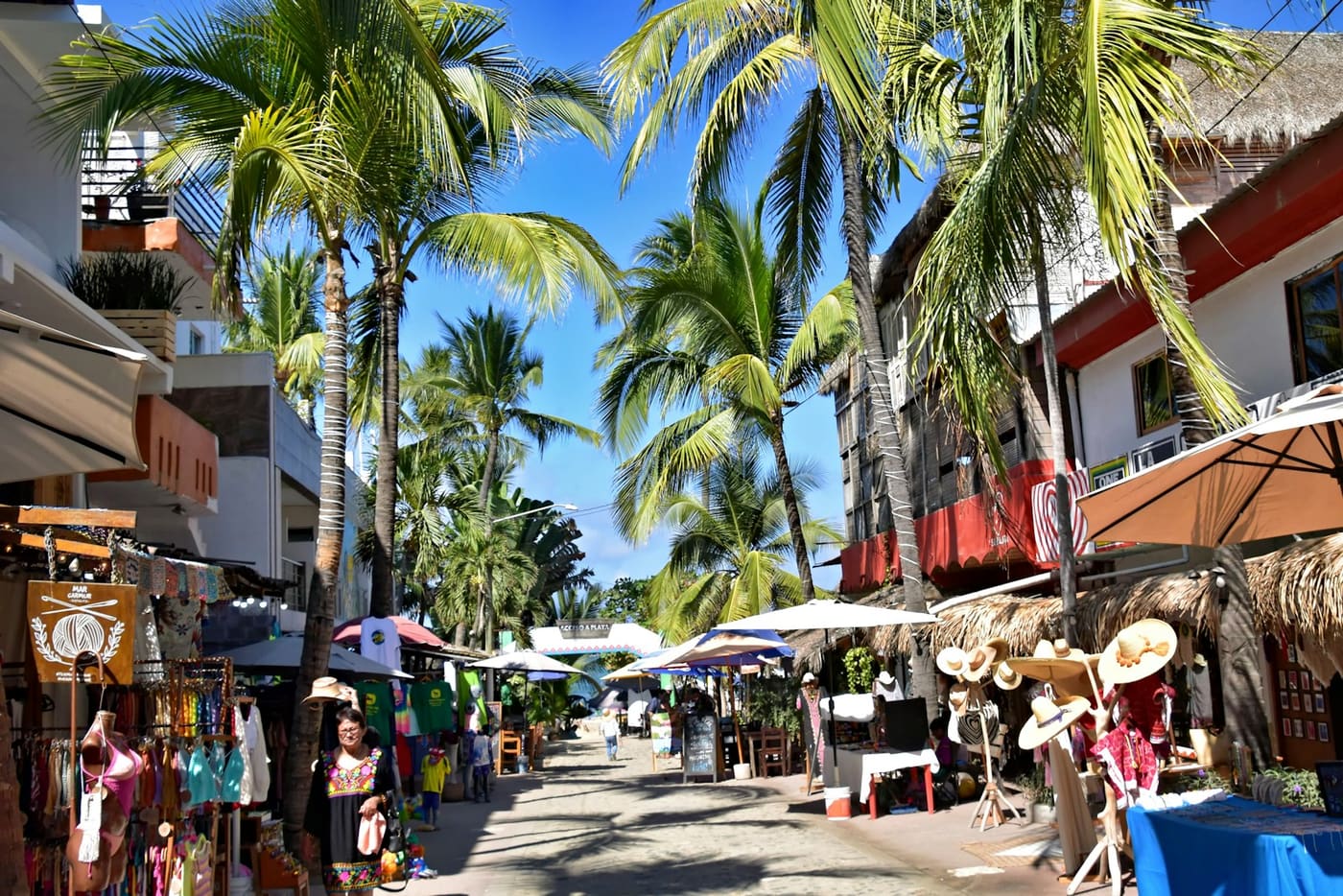 An open-air market street lined with shopfronts and palm trees.