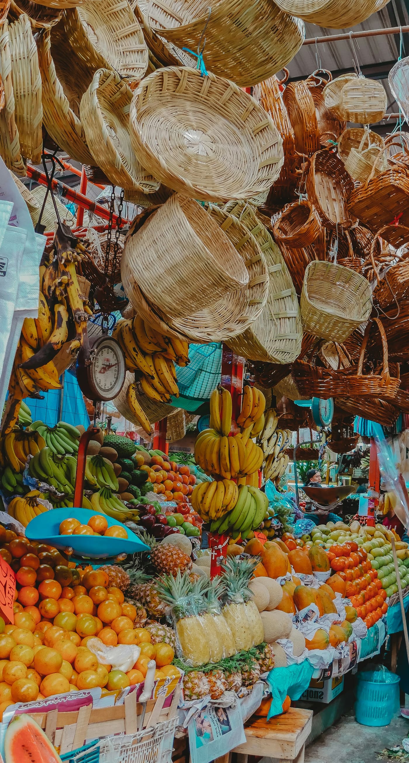 Woven baskets hanging above crates of oranges and other fruit at a market stall.