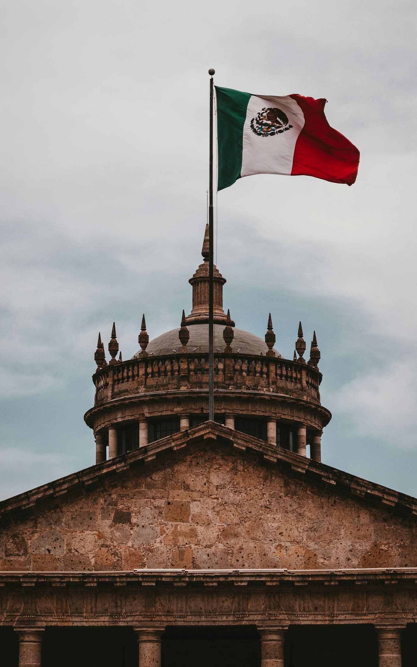 A Mexican flag flying from the top of a building against the sky.