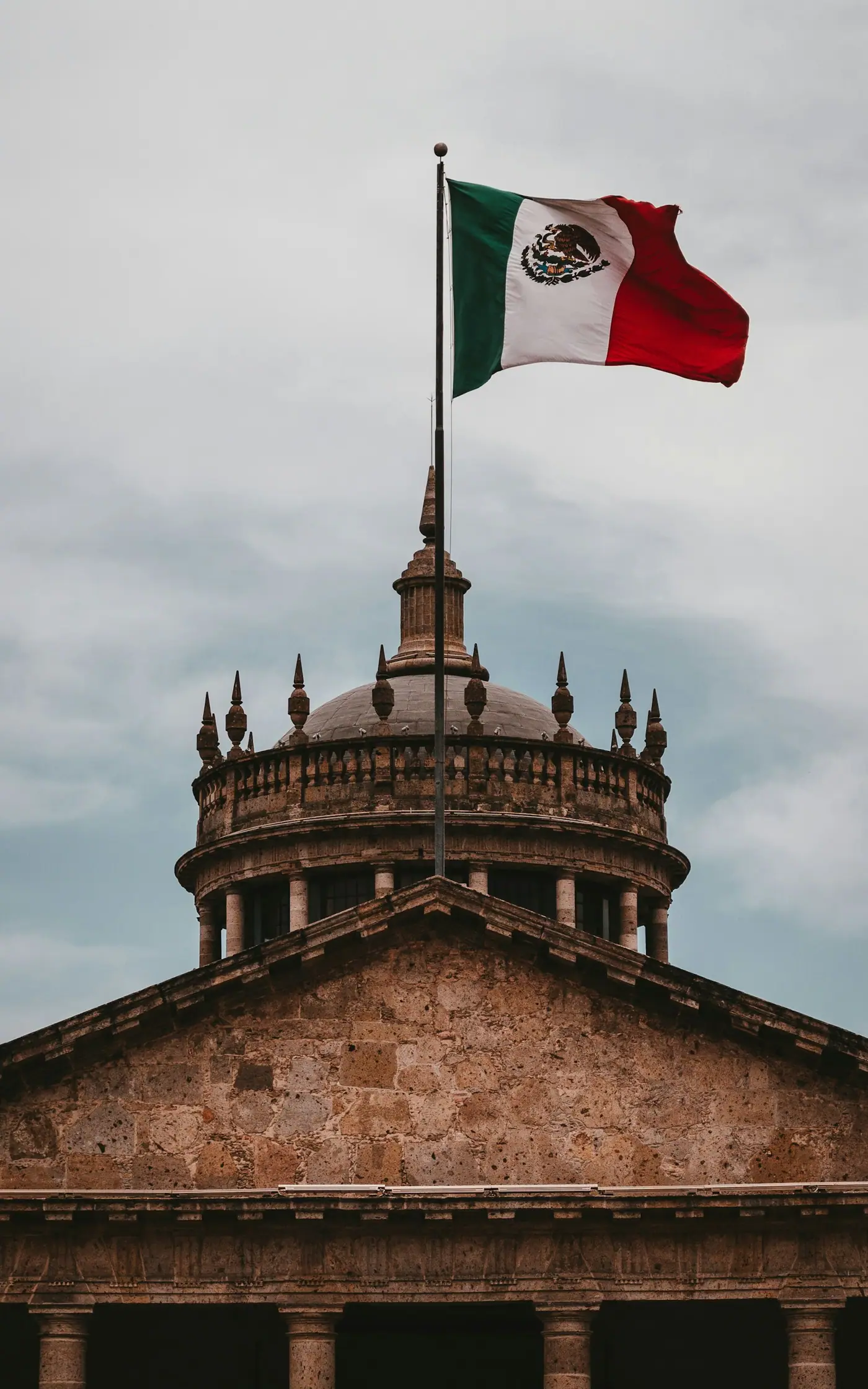 A Mexican flag flying from the top of a building against the sky.
