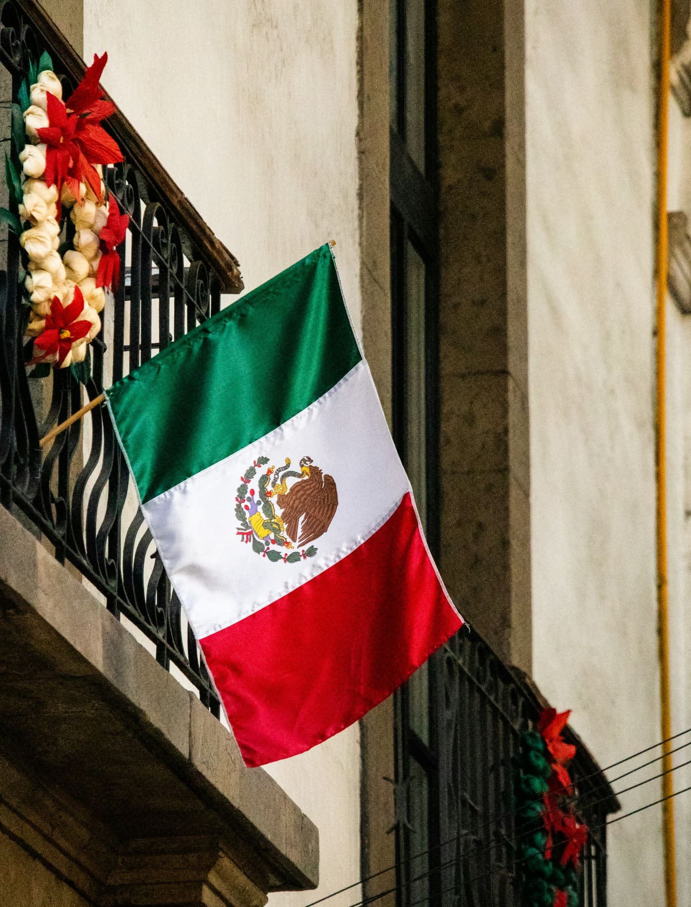 A Mexican flag hanging from the balcony of a building.
