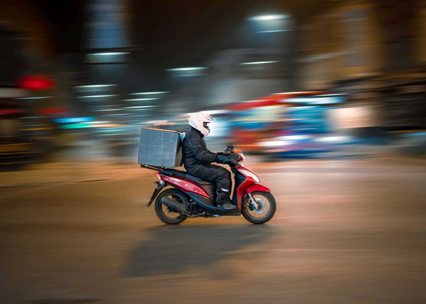 A delivery rider on a scooter blurred in motion on a Mexican street at night.