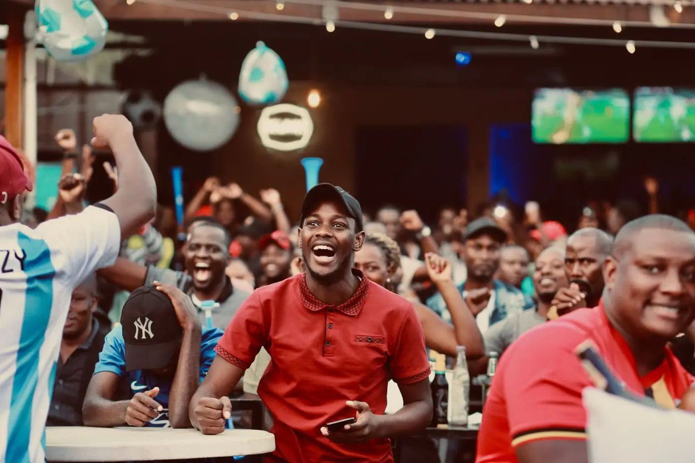 A crowded Mexican cantina with fans reacting in shock to a play on the screen.