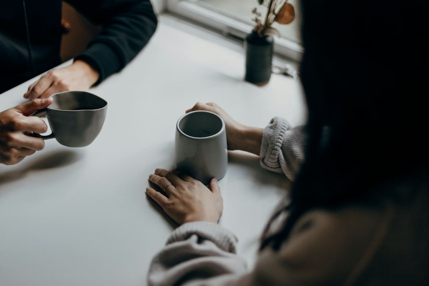 Two people talking over mugs of coffee at a table.