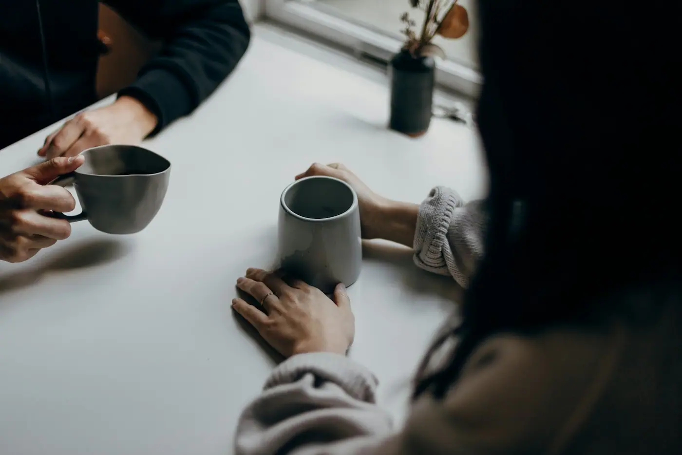 Two people talking over mugs of coffee at a table.