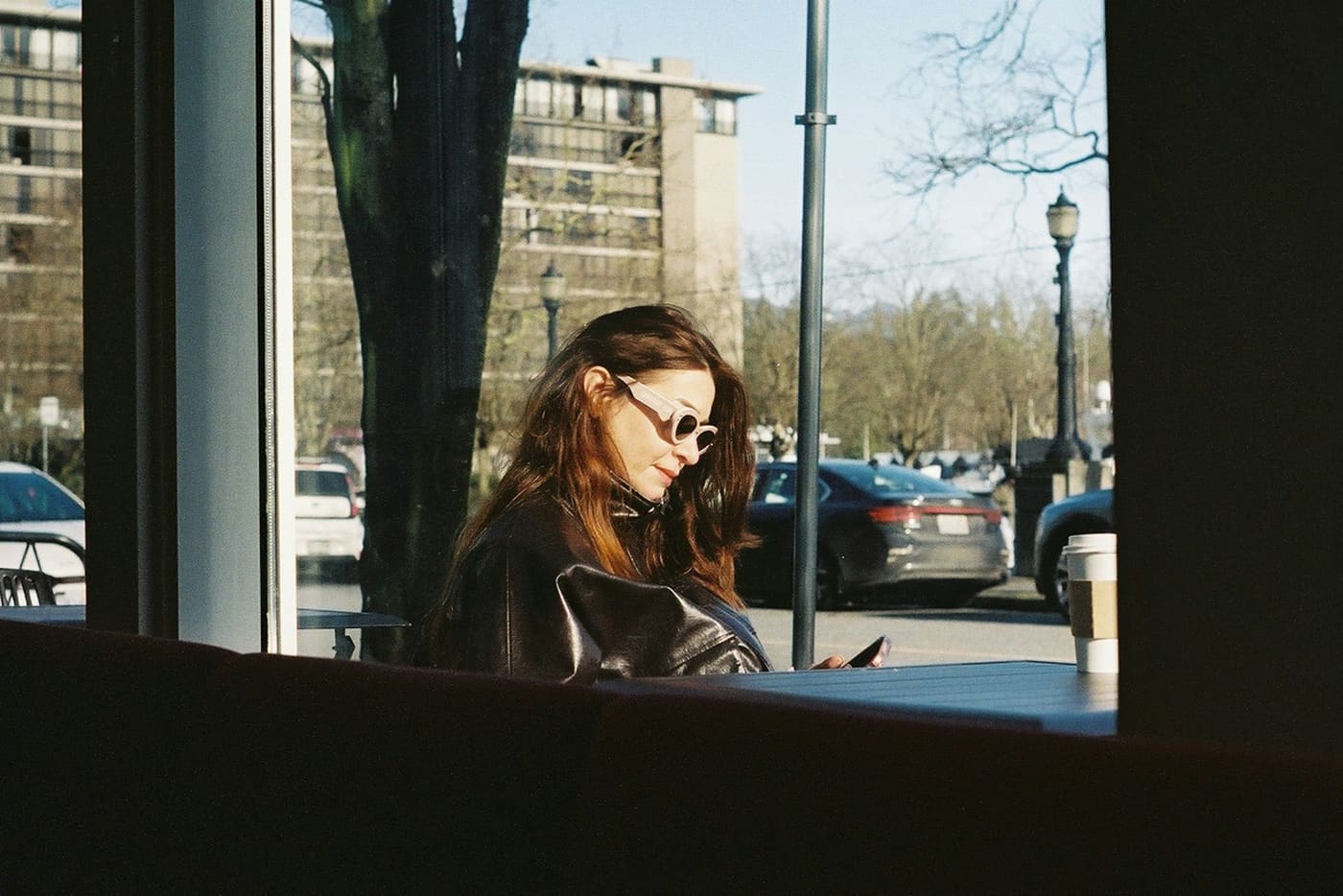 A woman looking at her phone inside a café window.