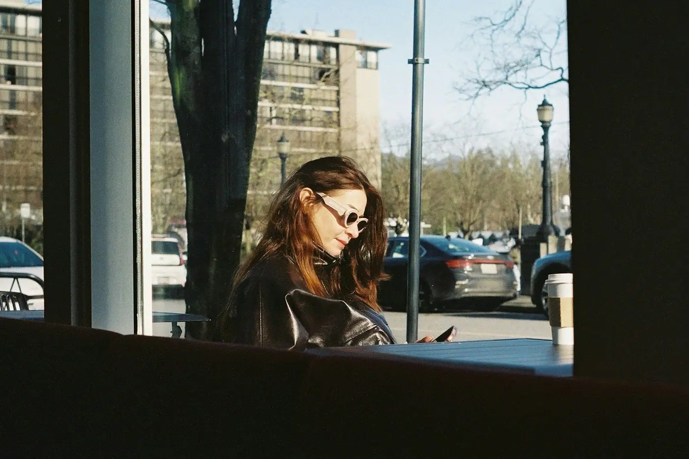 A woman looking at her phone inside a café window.