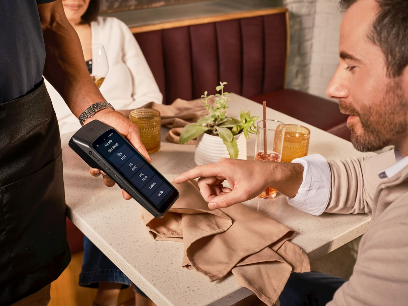 A waiter holding a card payment terminal towards a customer at a restaurant table.