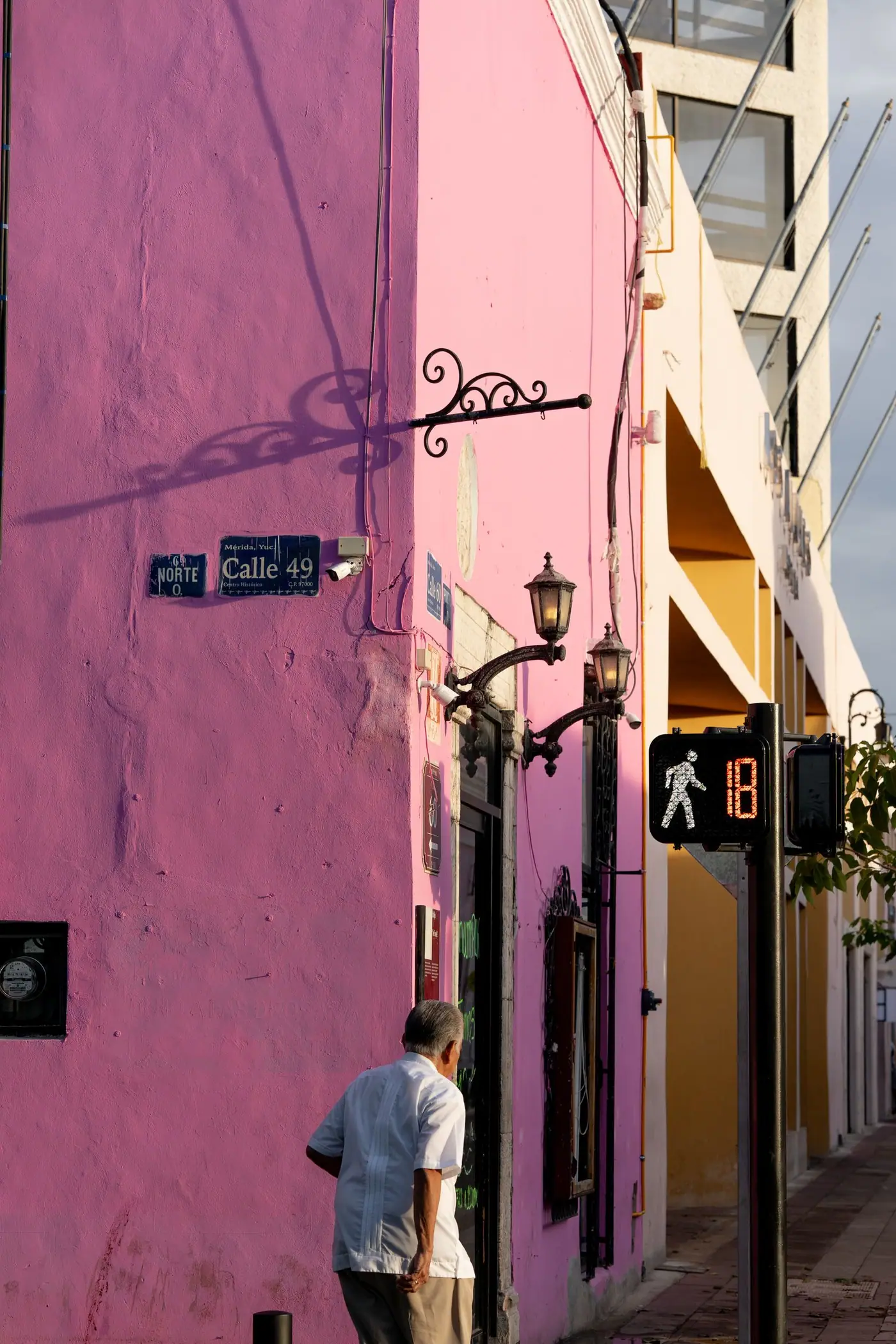 A man walking past a bright pink colonial building on Calle 49 in Merida.