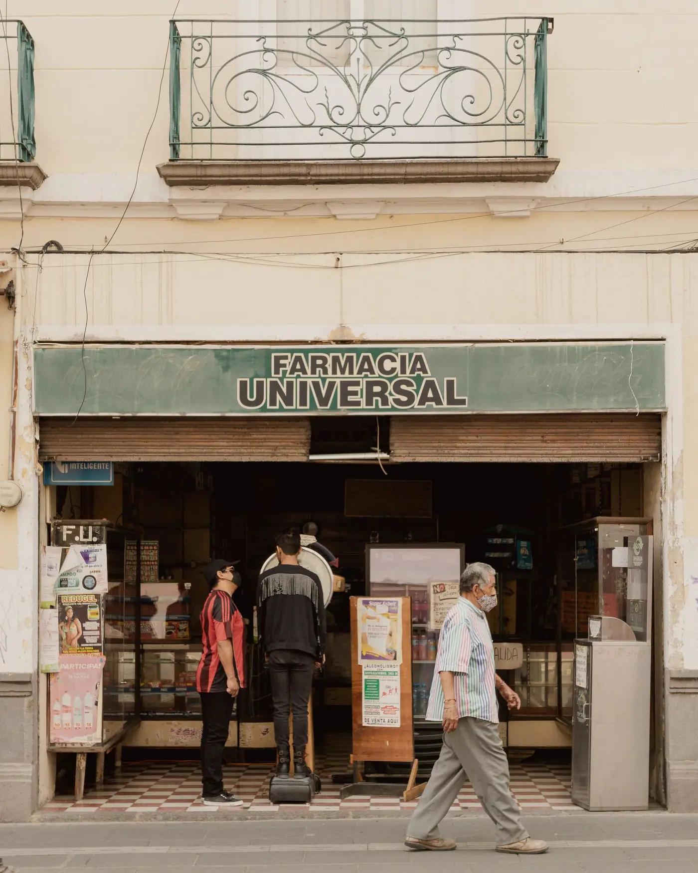 A pharmacy on a street corner in Mexico with a bright sign above the door.