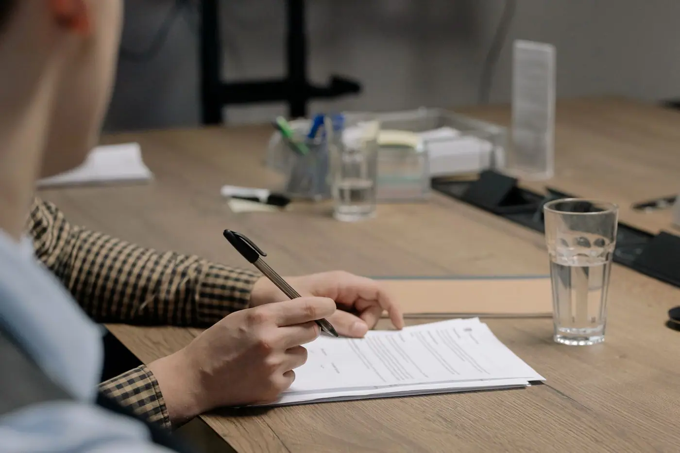 A person in business clothes signing a document at a wooden table.