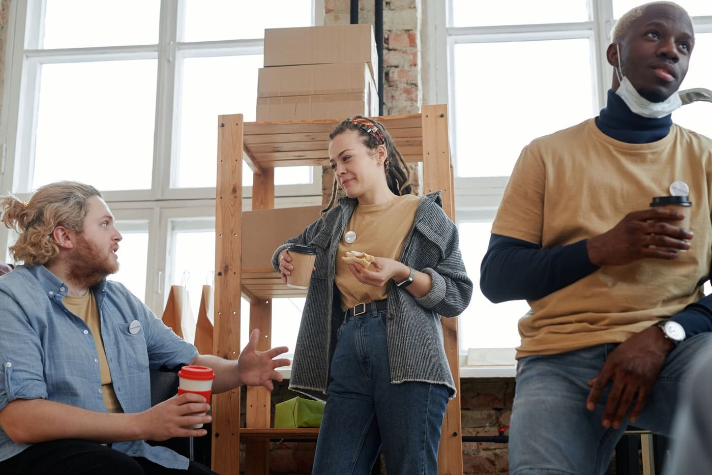 Three coworkers talking over coffee and snacks during a casual break.