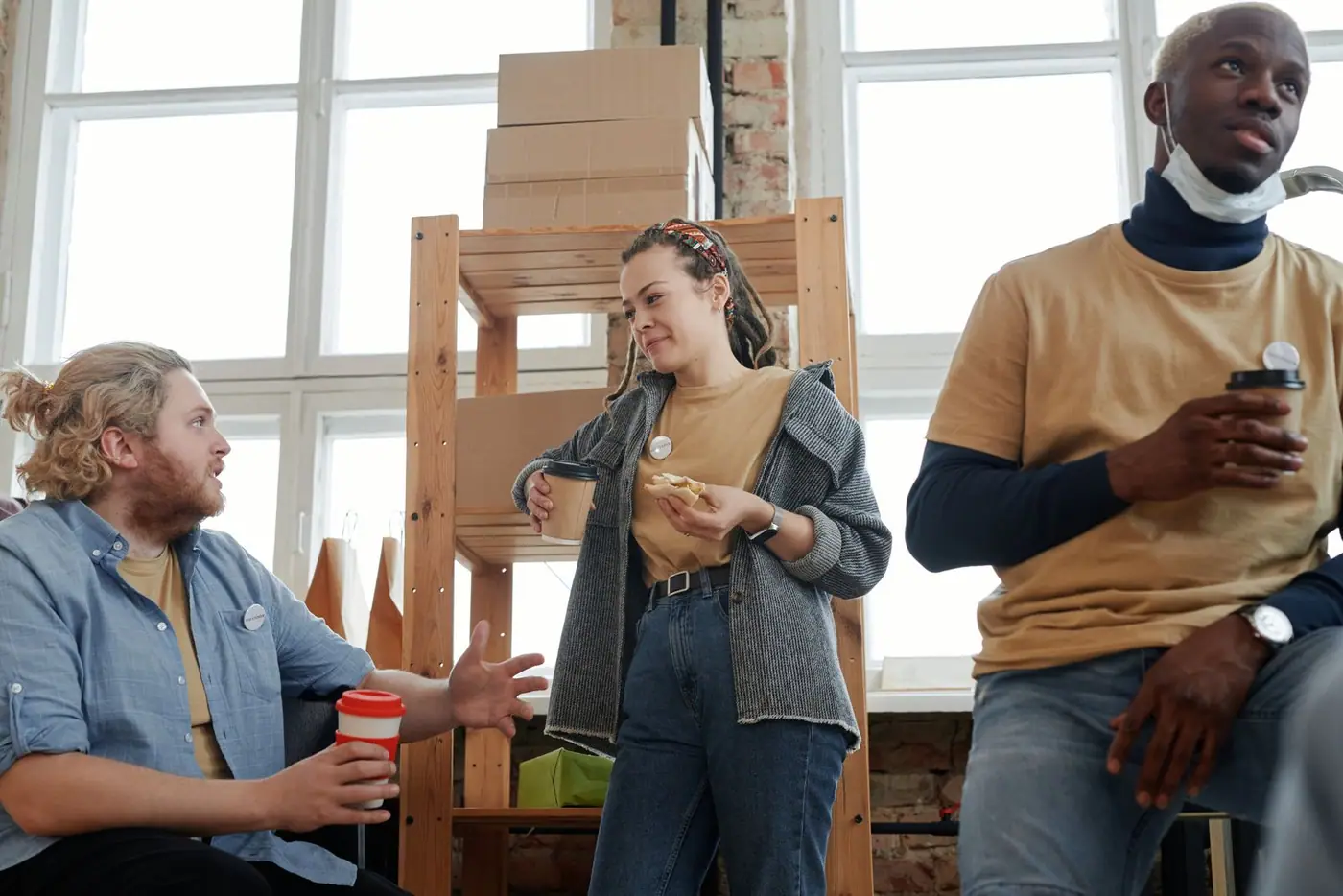 Three coworkers talking over coffee and snacks during a casual break.