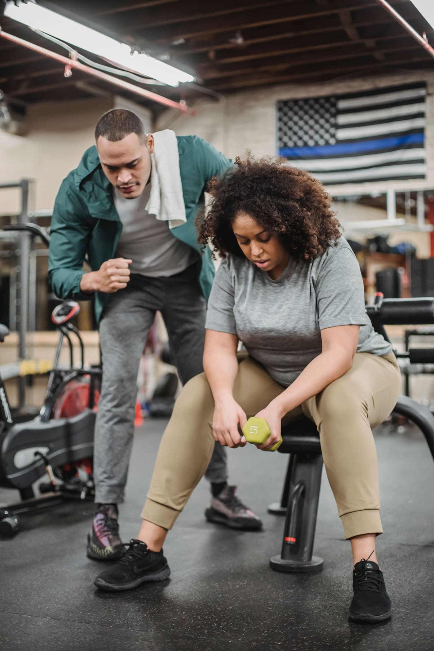 A personal trainer helping an adult exercise safely with a dumbbell.